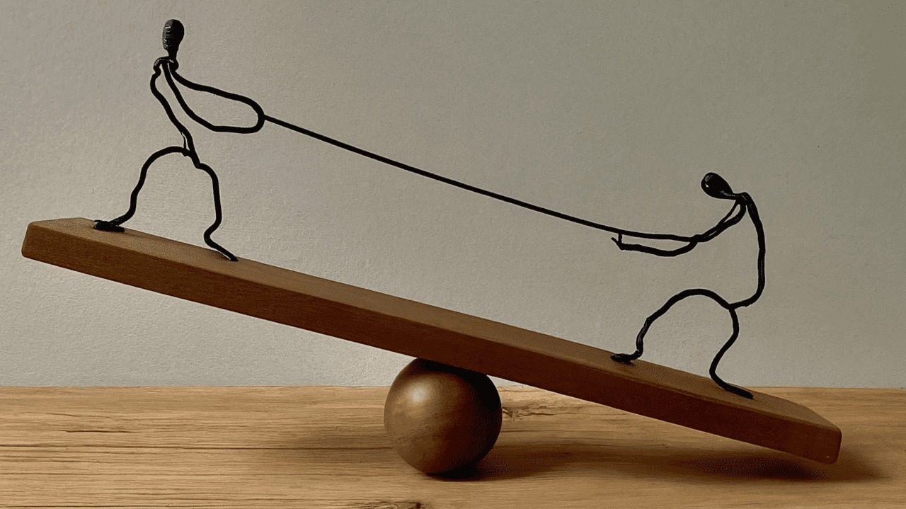 Stick figures having a tug of war on a seesaw.